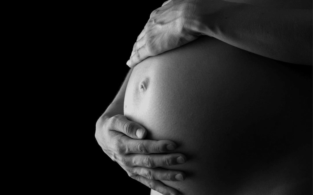 Black and white shot of hands holding pregnant belly.