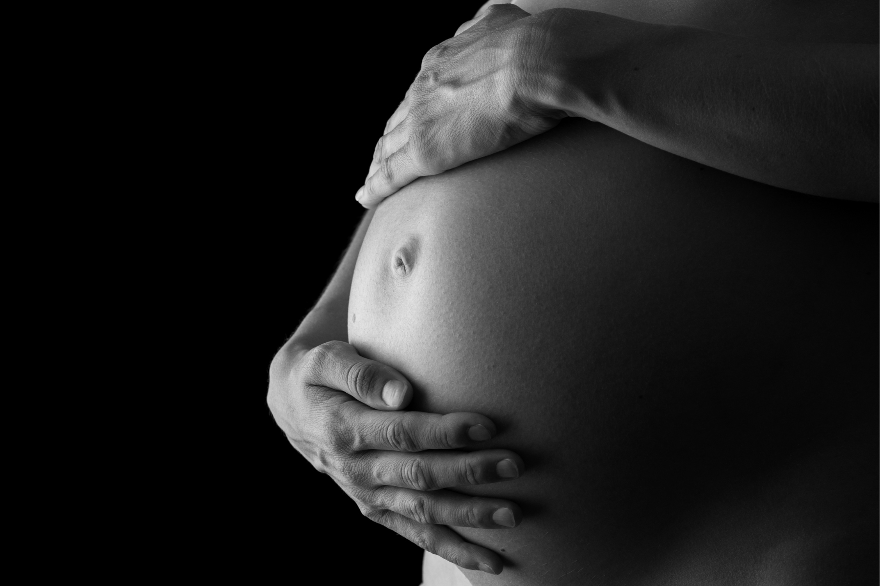 Black and white shot of hands holding pregnant belly.